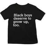 A black short-sleeve t-shirt with the text 'Black boys deserve to grow up, too.' printed in white sans-serif font across the chest, shown against a plain white background.