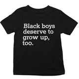 A black short-sleeve t-shirt with the text 'Black boys deserve to grow up, too.' printed in white sans-serif font across the chest, shown against a plain white background.